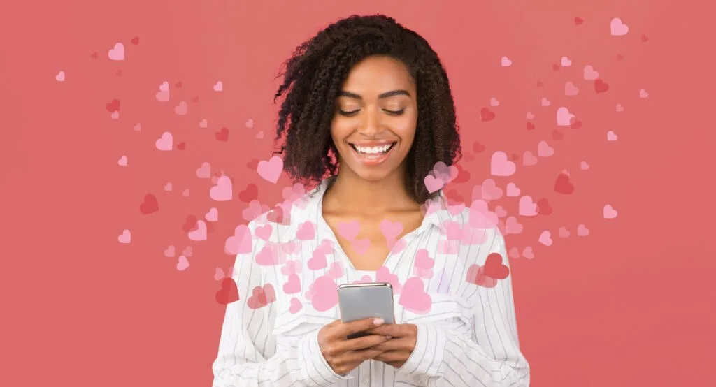 Mulher afro-americana navegando pelas mídias sociais no celular com corações voando ao redor, fundo rosa | ThirstyAffiliates